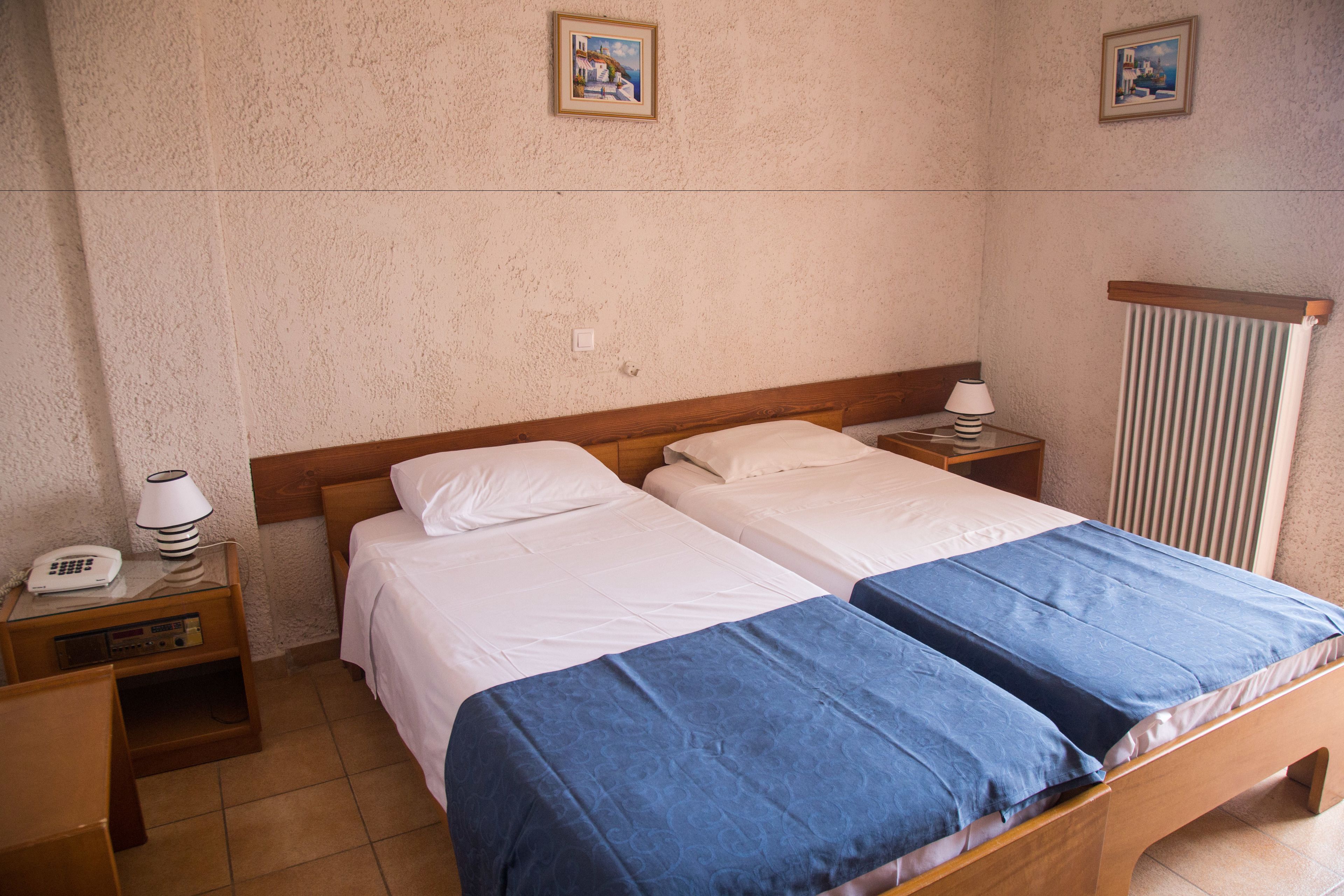 Een tweepersoonsbed met wit en blauw beddengoed, een houten hoofdbord, nachtkastjes met lampen en een radiator aan de muur.