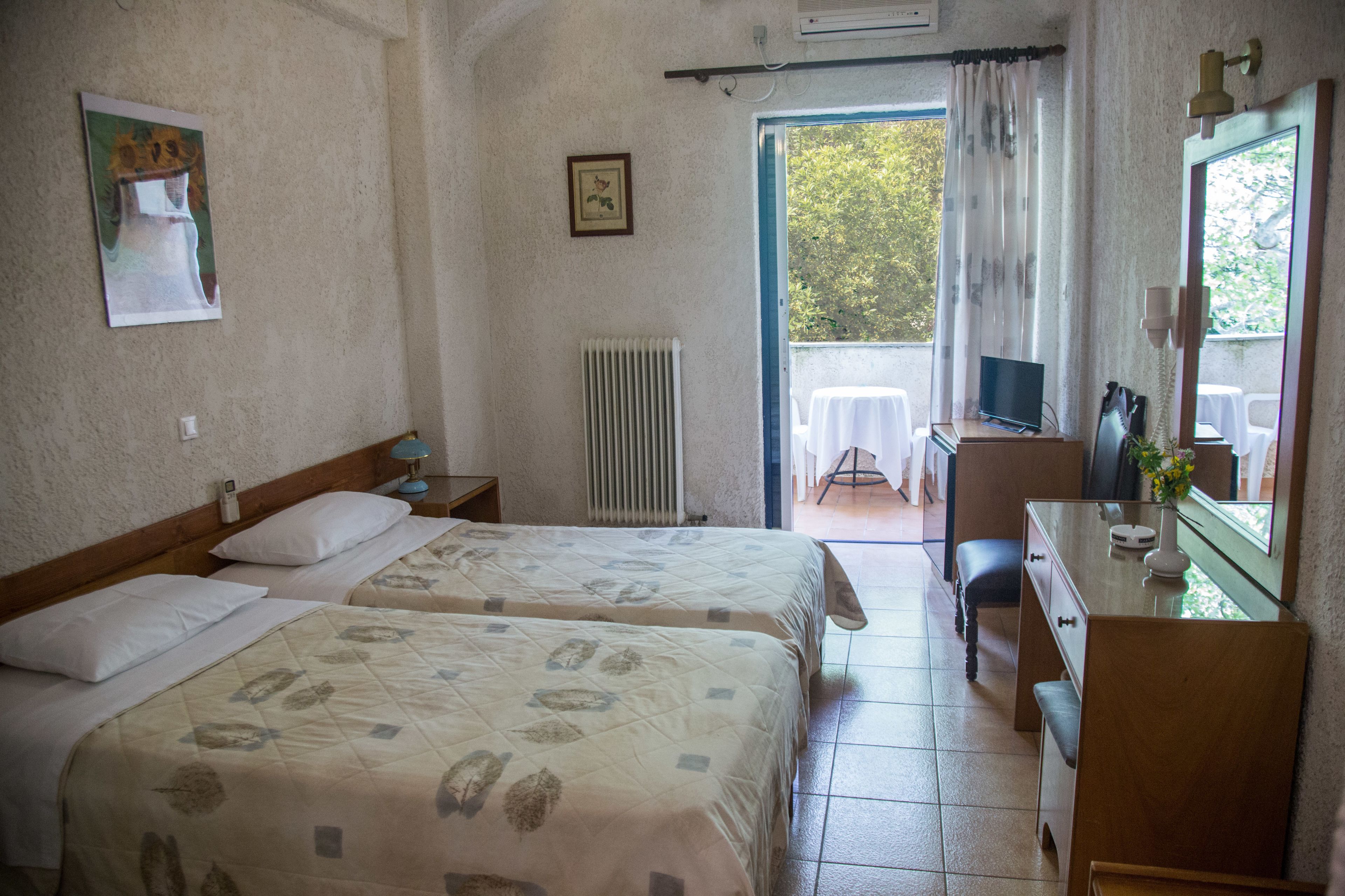 Ein Hotelzimmer mit zwei Betten, einem Schreibtisch mit Fernseher, einer Heizung und einem Balkon mit Tisch und Stühlen.