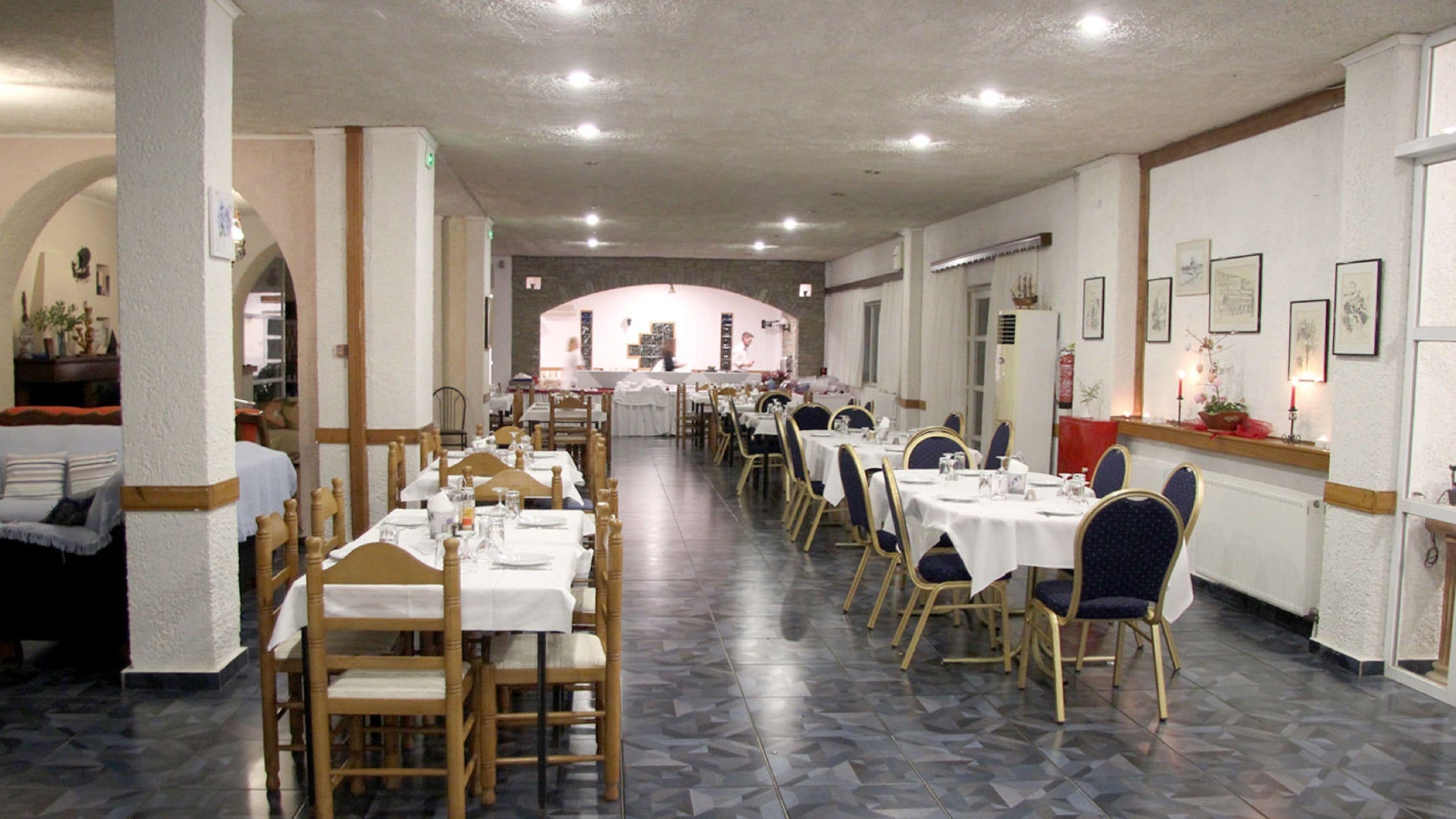A dining area with multiple tables and chairs, a tiled floor, and framed pictures on the walls.