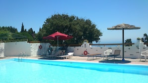 Un área de piscina con una piscina azul cristalina, sillas de descanso y una sombrilla roja.