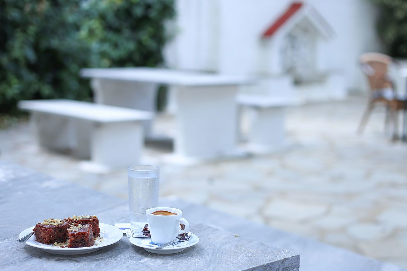 A table with a plate of food and a cup of coffee, set against a backdrop of outdoor seating and greenery.