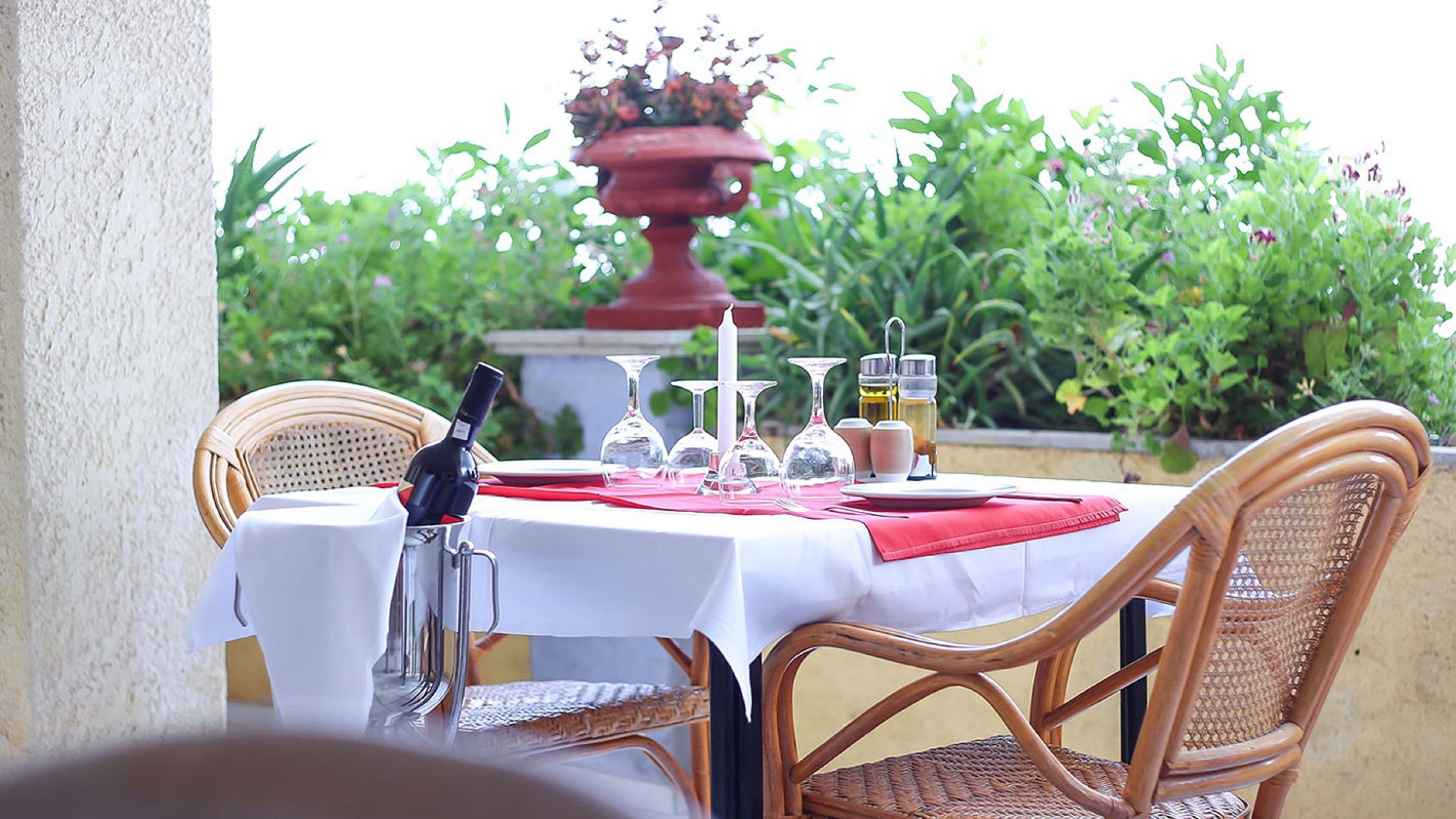 A table set for dining outdoors with wicker chairs, a white tablecloth, and a red napkin.