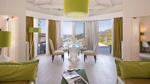 A spacious room with a dining table and chairs, large windows with curtains, and a view of a landscape. - Salvator Villas & Spa Hotel (Parga)