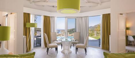 A spacious room with a dining table and chairs, large windows with curtains, and a view of a landscape.