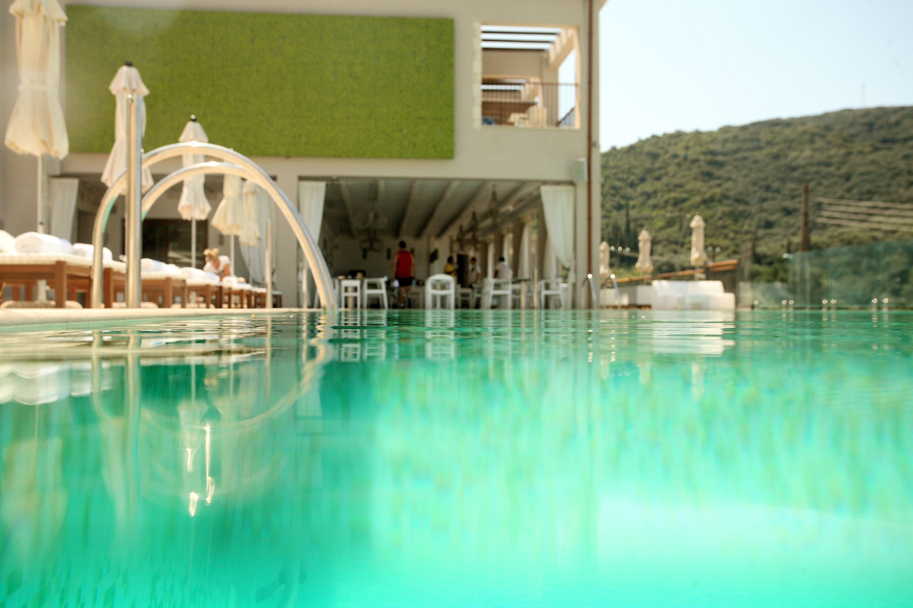 A swimming pool with clear water, surrounded by lounge chairs and umbrellas, and a building with a green wall and balconies in the background.