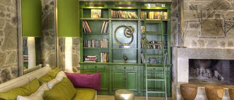 A cozy living room with a green bookshelf, a fireplace, and a white sofa with green and purple cushions.