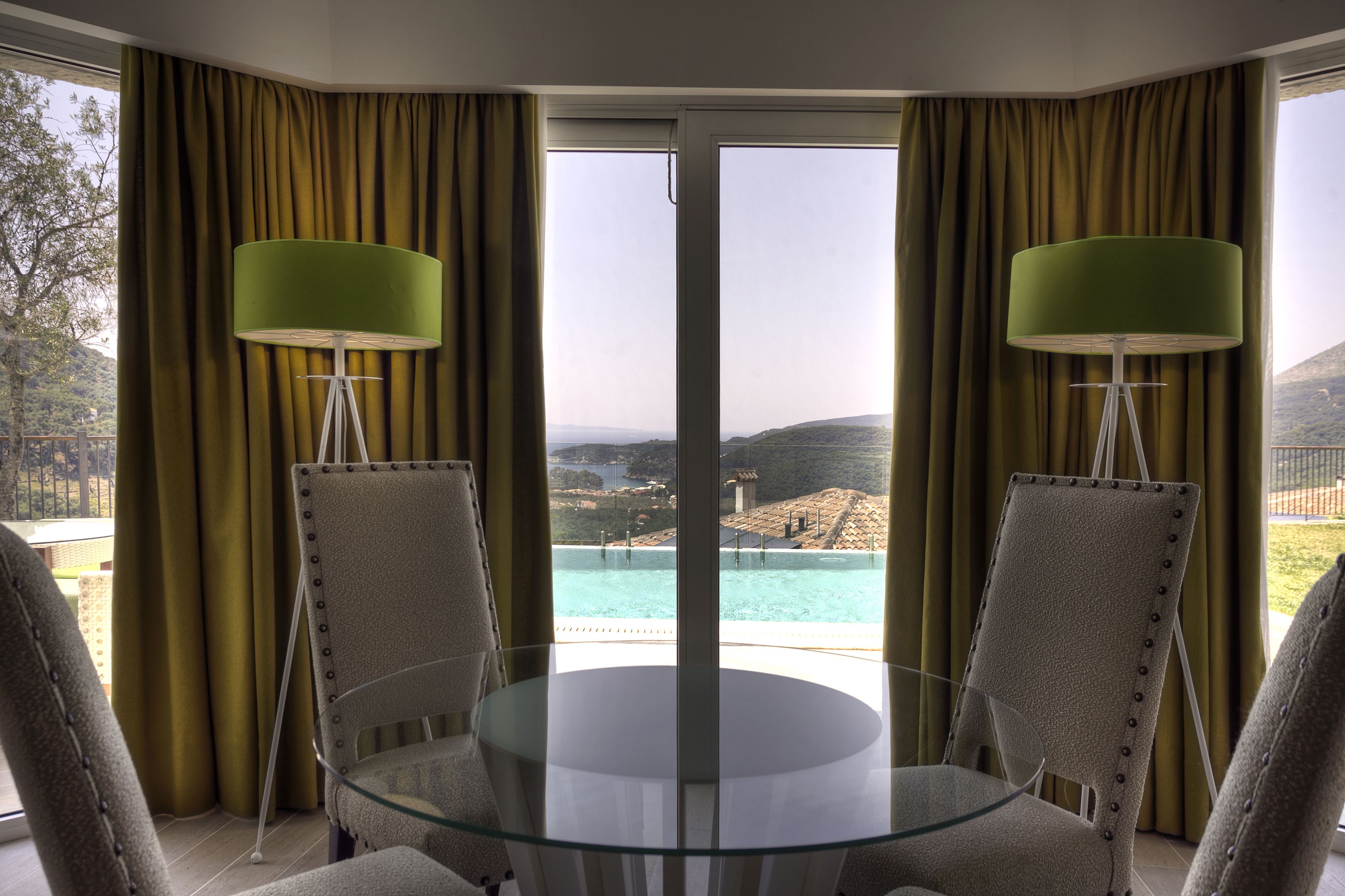 Una stanza con tavolo in vetro, due sedie, vista su una piscina e tende.