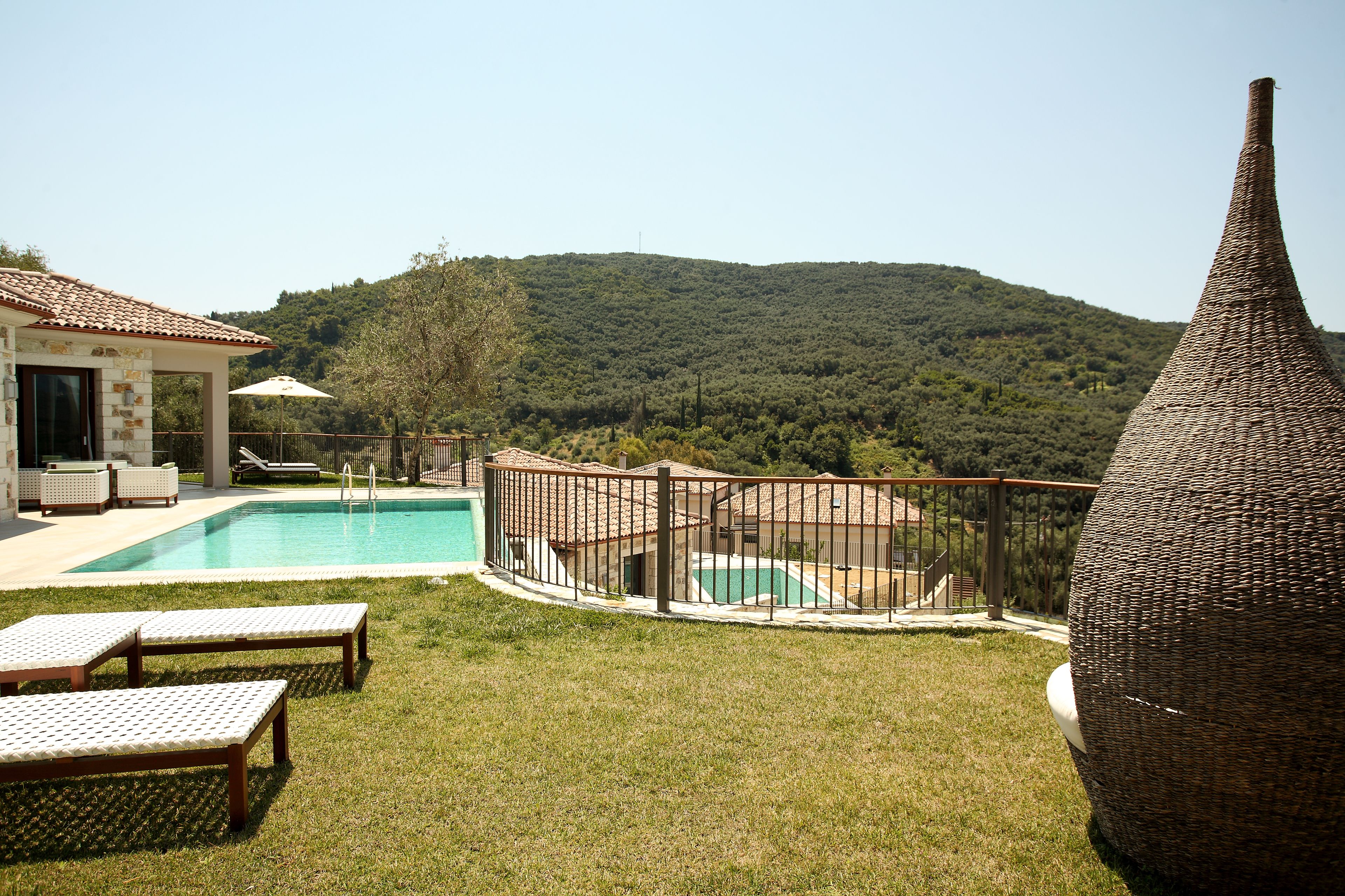 Un área de piscina con sillones de descanso, una terraza cercada y vistas a una colina boscosa.