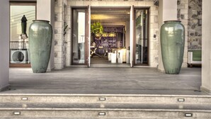 A modern building entrance with large green vases, stone walls, and a well-lit interior with bookshelves and seating. - Salvator Villas & Spa Hotel (Parga)
