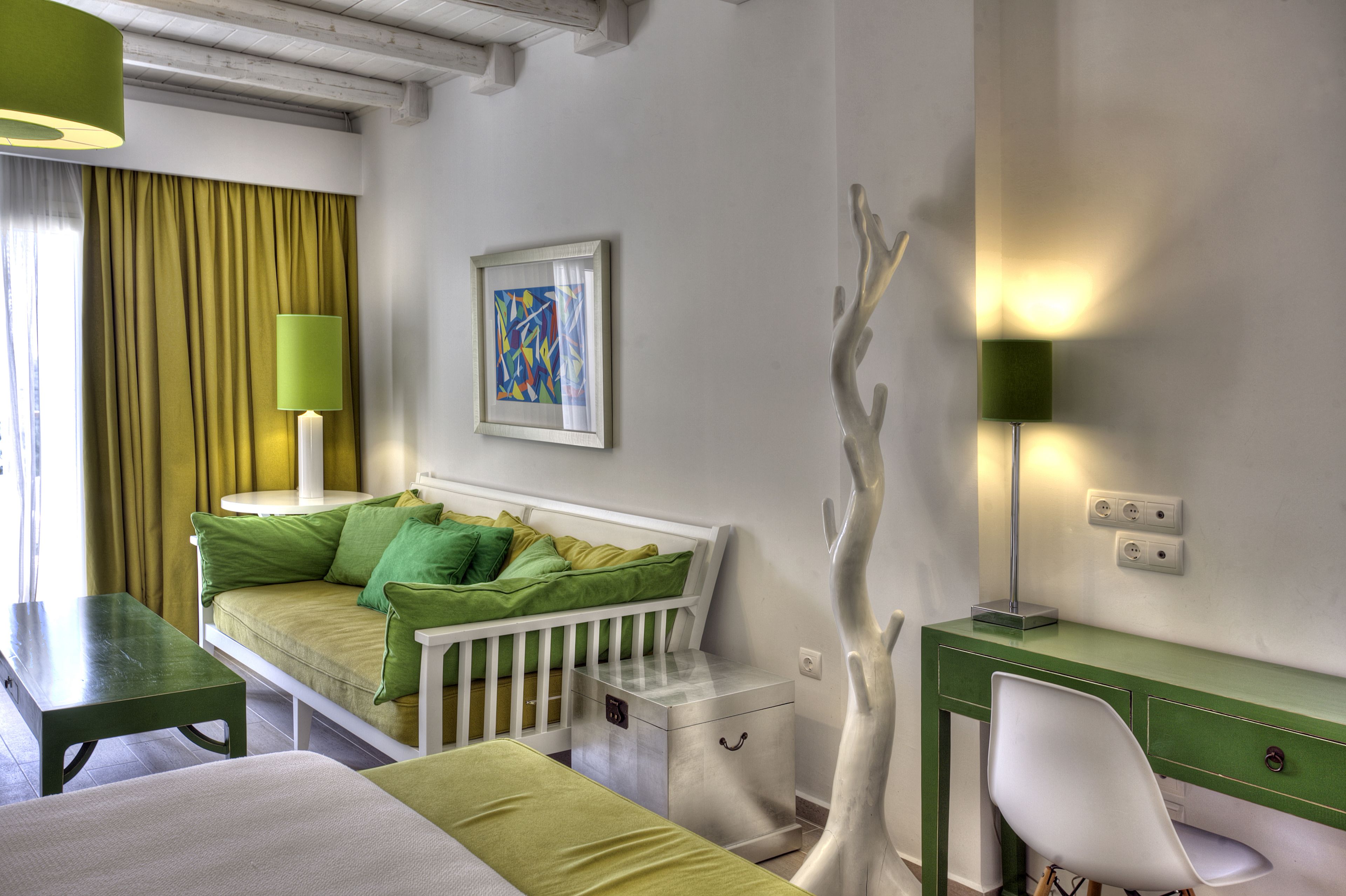 Una habitación con un sofá verde, una cuna blanca, un escritorio y una lámpara.