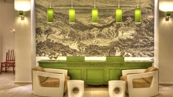 A reception area with a green counter, two white armchairs, and a mural of a mountainous landscape.