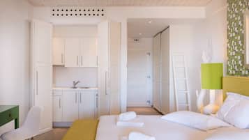 Ein Hotelzimmer mit Bett, Schreibtisch, Stuhl, einer grünen Bank, einem Waschbecken und einem Spiegel.