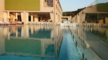 An infinity pool with clear water, surrounded by white lounge chairs and tables, and a building with a green wall and balcony overlooking the pool.