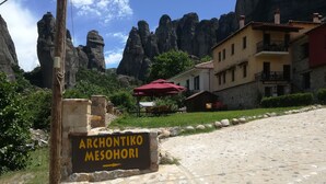 A sign for Archontiko Mesohori with a stone pathway leading to a building with a red awning. - Archontiko Mesohori (Kalabaka)
