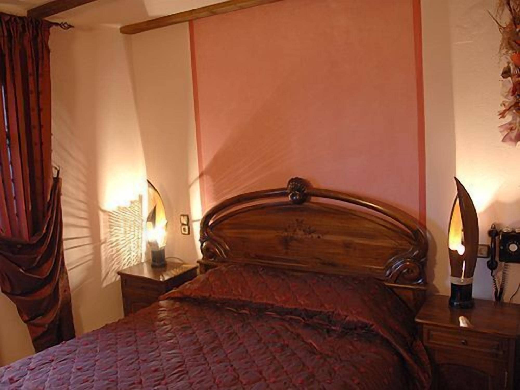 Un dormitorio con una cama de madera, una mesita de noche con una lámpara y un espejo montado en la pared.