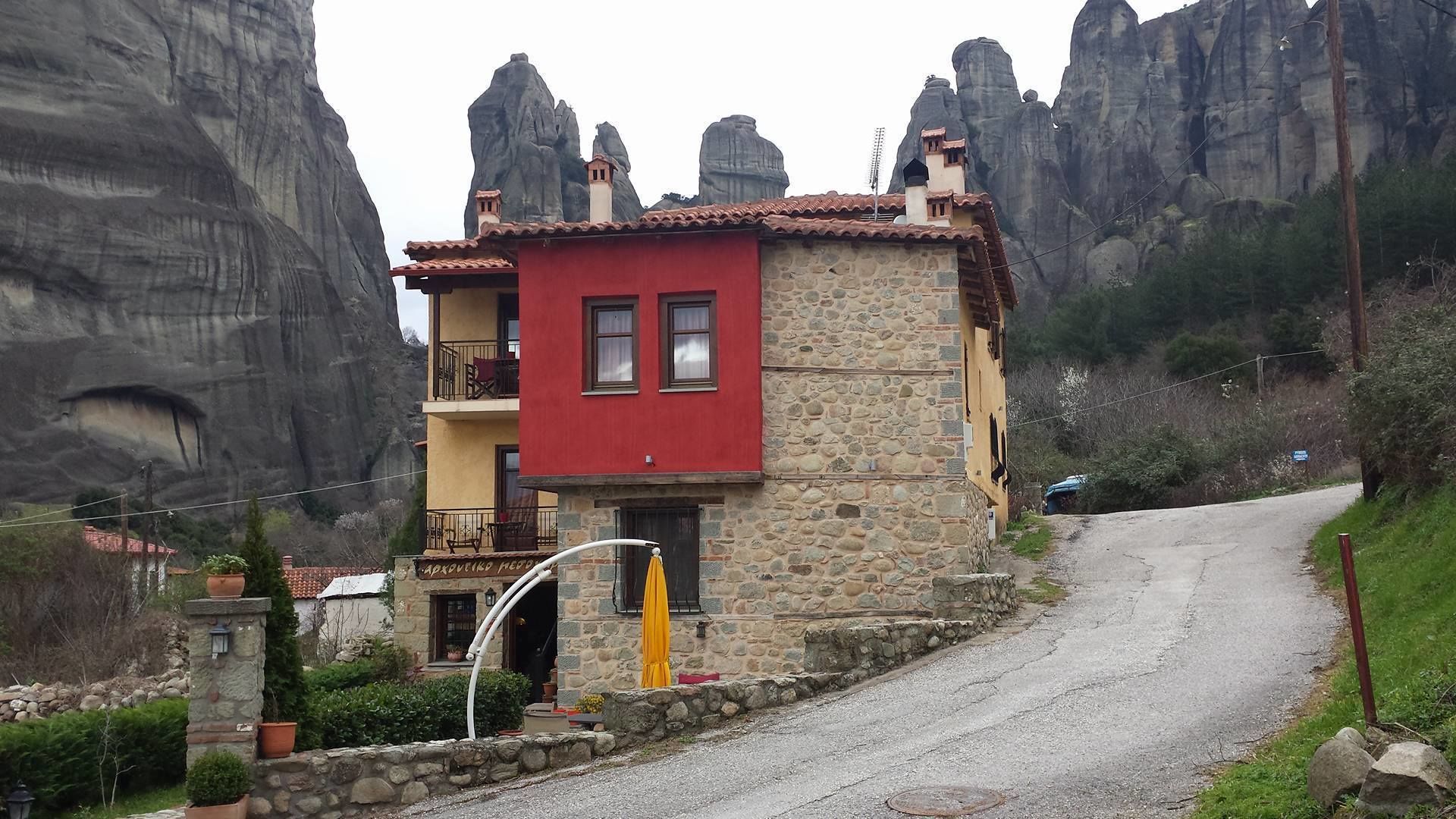 A two-story building with a red upper floor and a stone lower floor, situated on a gravel road with a yellow umbrella and a stone lantern in the foreground.