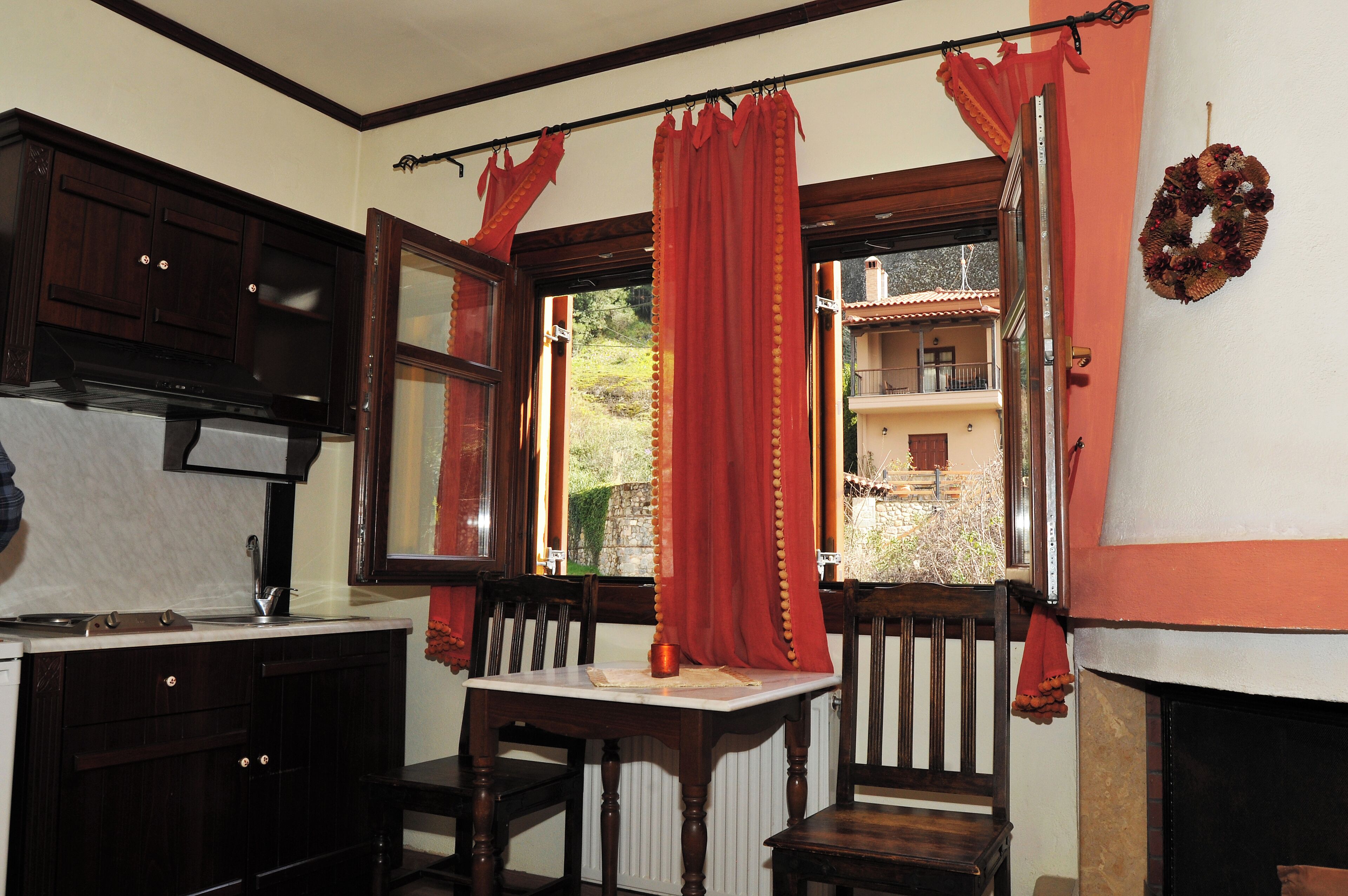 Un comedor con una mesa y sillas, una ventana con cortinas rojas y vistas a un edificio.