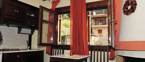 A dining area with a table and chairs, a window with red curtains, and a view of a building outside.
