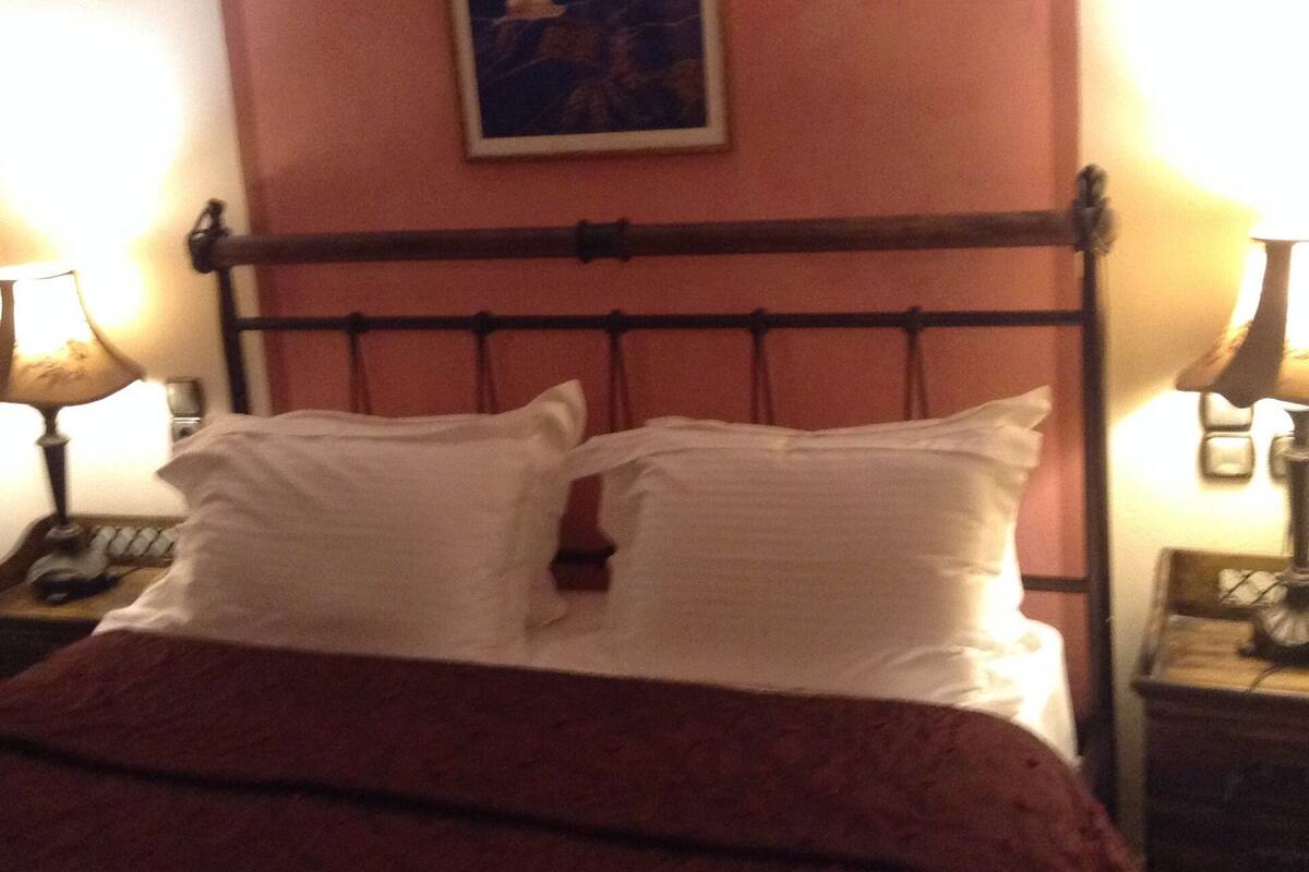 Ein Bett mit Holz-Kopfteil, zwei Nachttische mit Lampen und ein an der Wand hängendes Bild.