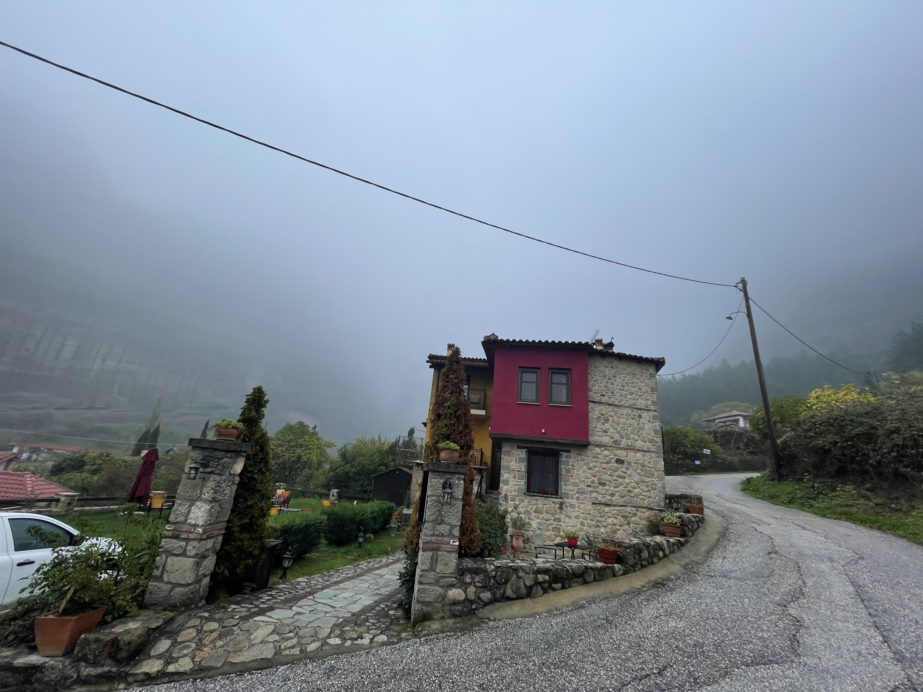 Una casa in pietra con una sezione superiore rossa e una sezione inferiore in pietra, circondata da piante in vaso e un vialetto sterrato.