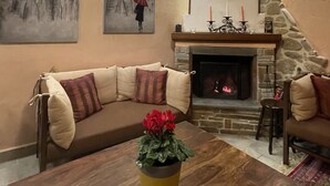 A cozy living room with a stone fireplace, a wooden coffee table with a yellow vase, and a beige sofa with patterned cushions. - Archontiko Mesohori (Kalabaka)