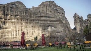 A patio with outdoor seating and a large rock formation in the background. - Archontiko Mesohori (Kalabaka)