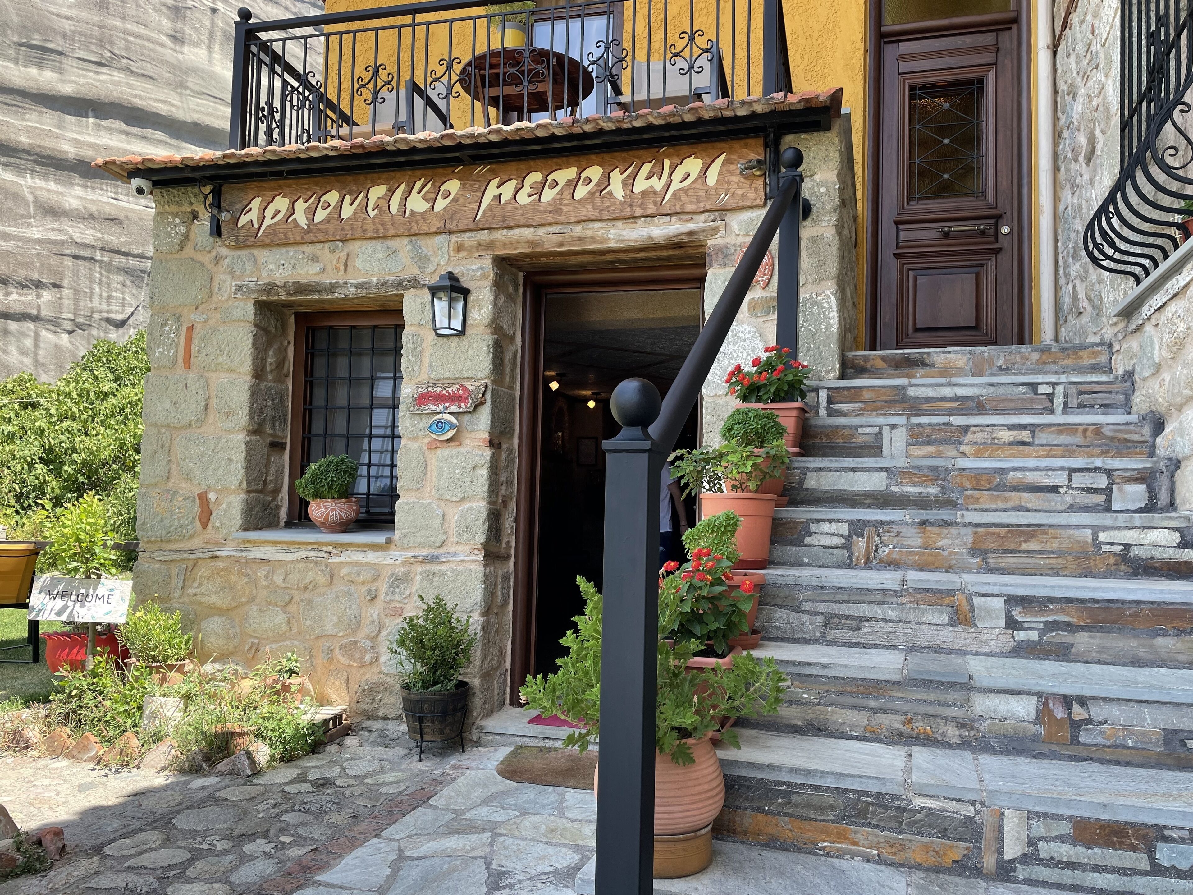 A stone building with a wooden sign reading "Apolovik Nedoxwpi".