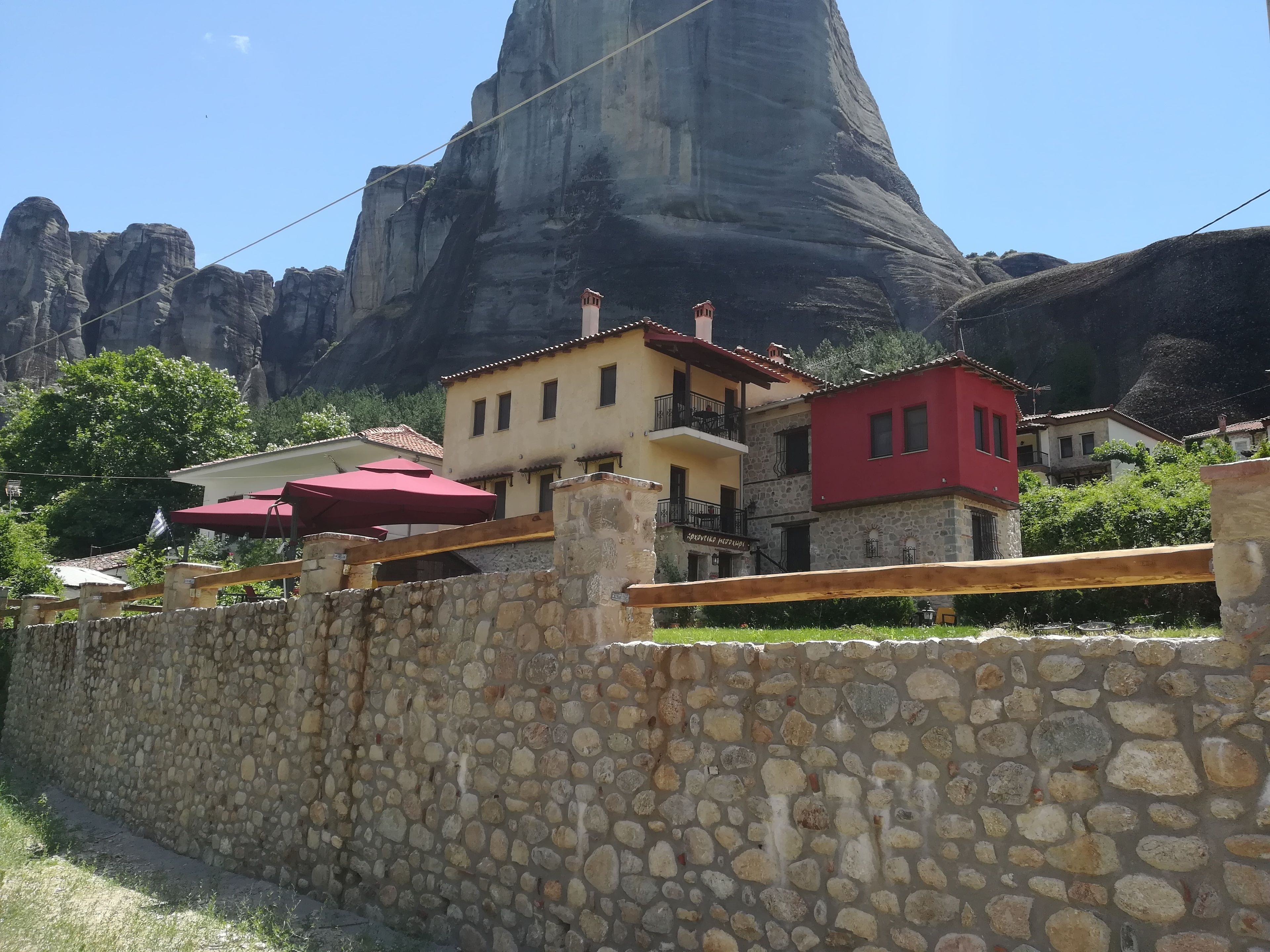 A stone wall with a stone building behind it, a red-roofed building to the right, and a large rock formation in the background.