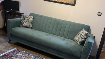 A living room with a teal sofa, patterned pillows, a colorful rug, and a wall-mounted abstract painting.