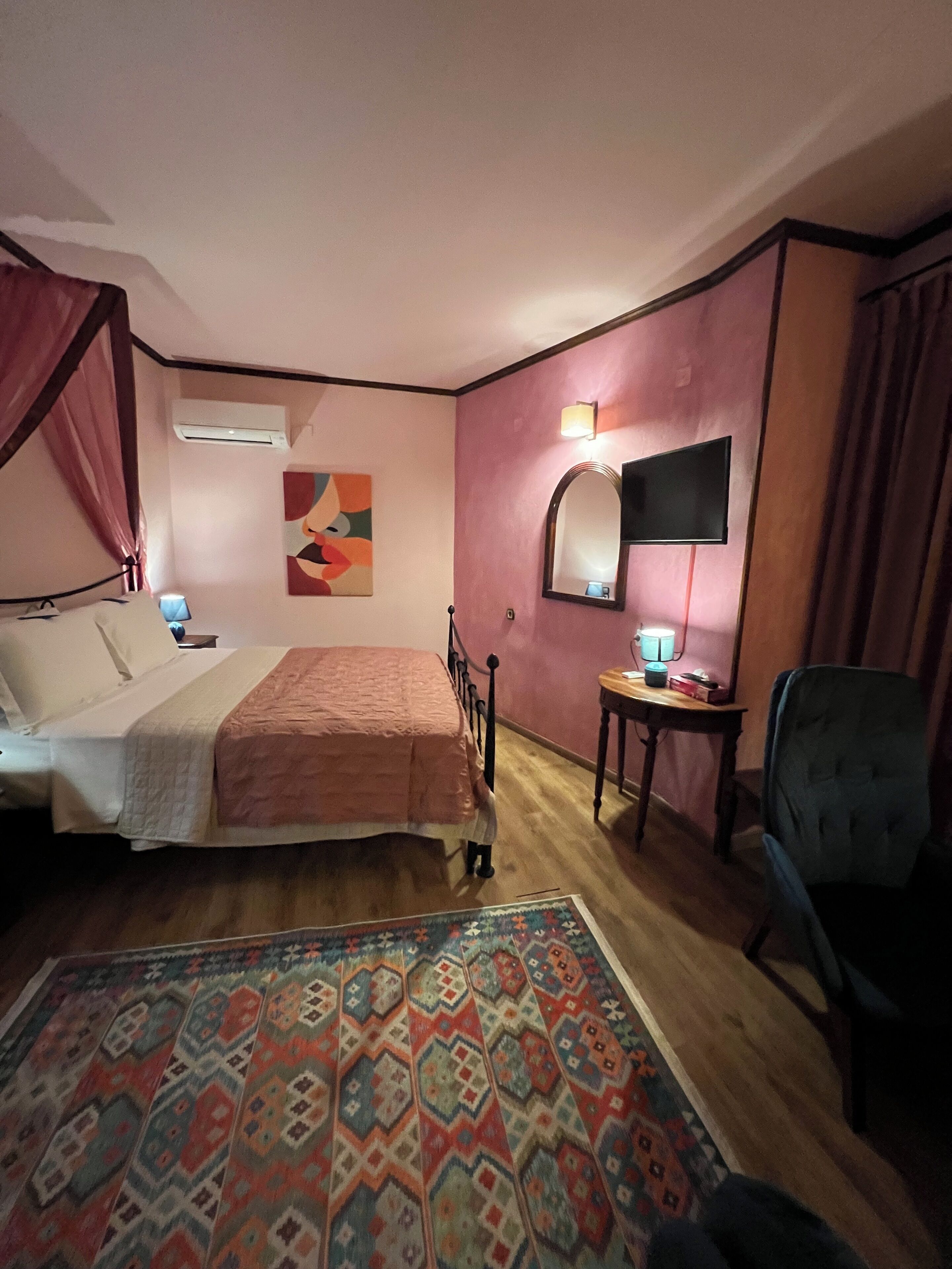 A bedroom with a bed, a desk, a chair, a TV, and a patterned rug.