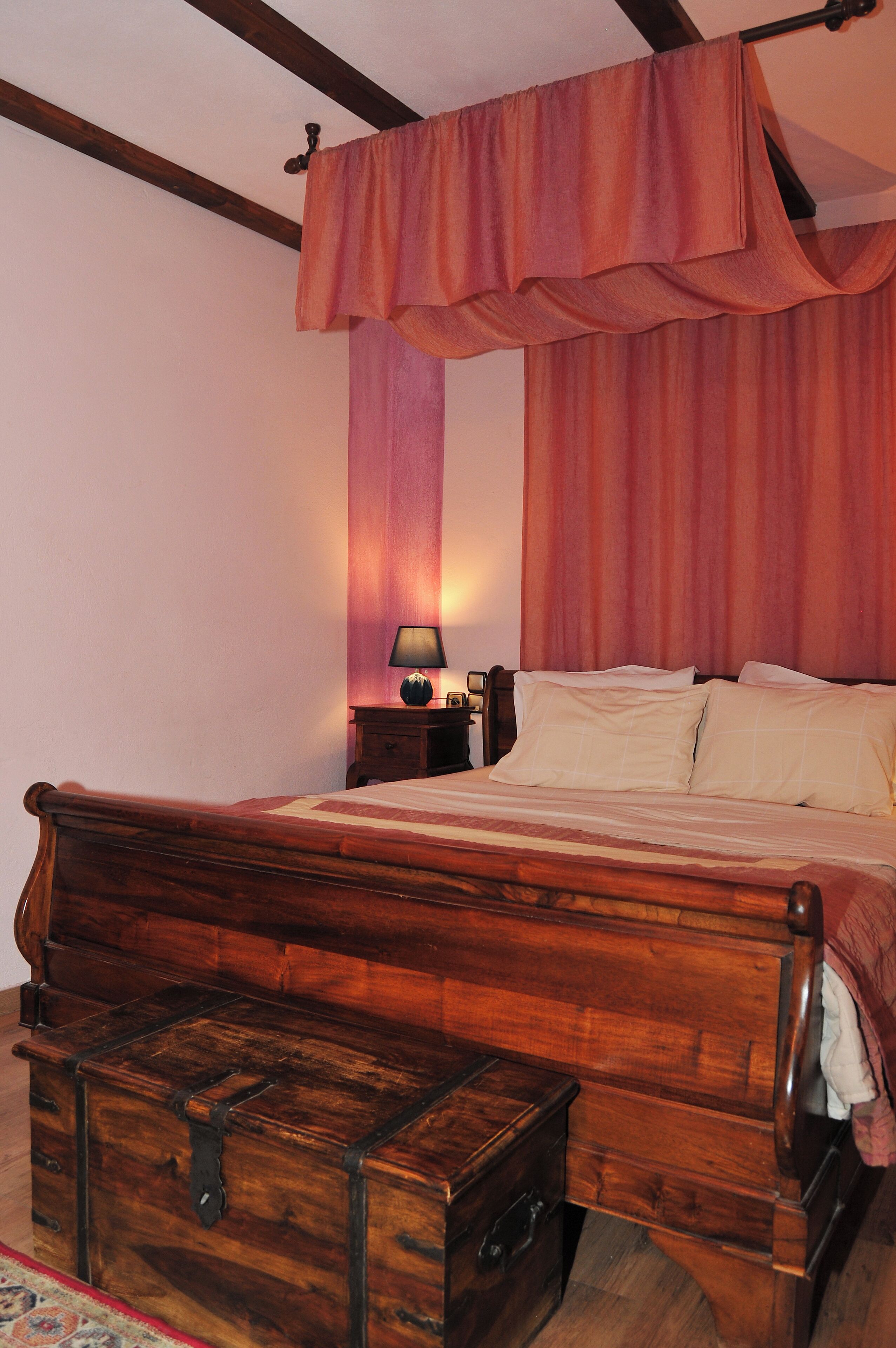 Ein hölzernes Bett mit Baldachin, ein Nachttisch mit Lampe und eine Kommode.