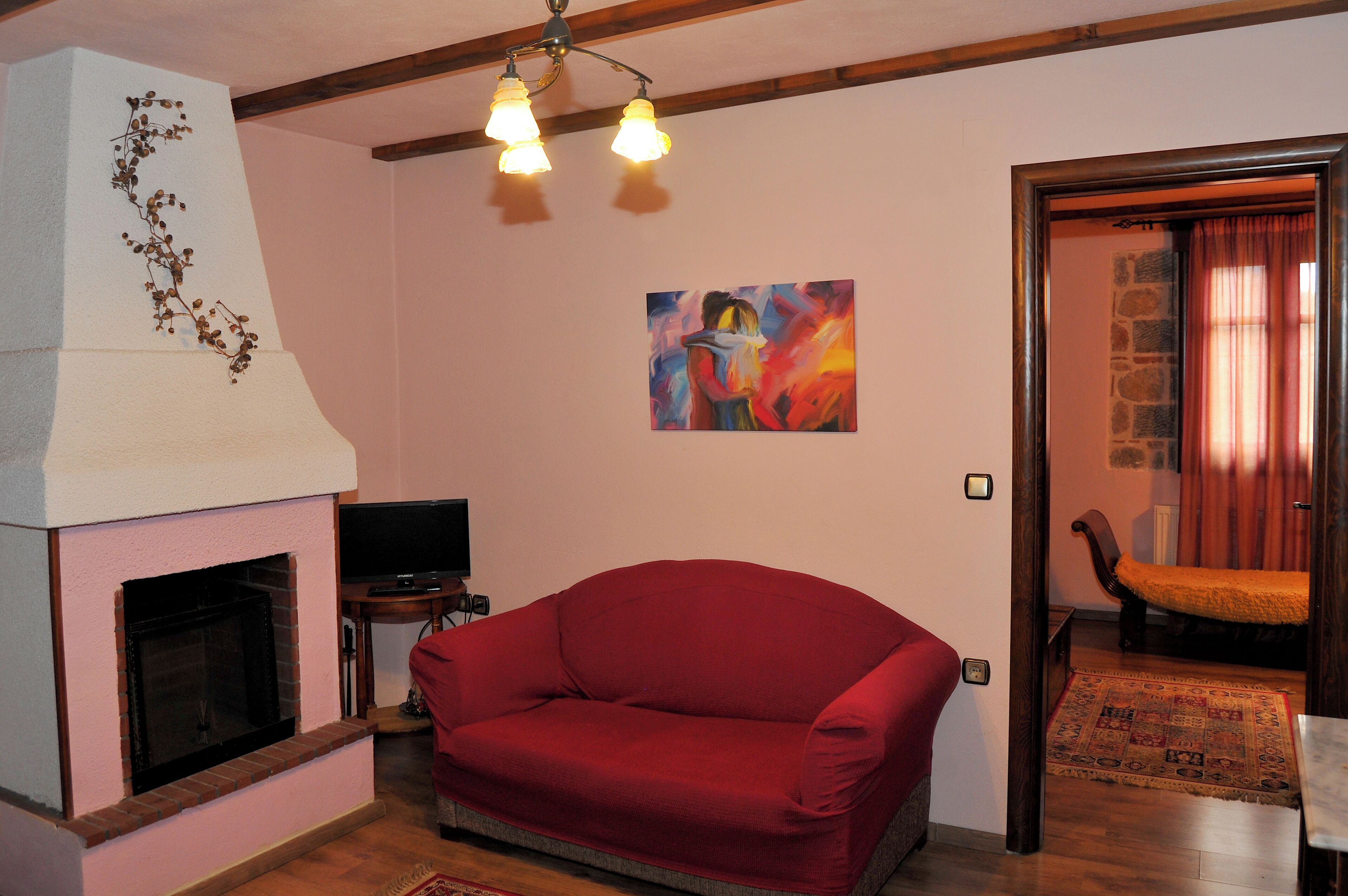 A living room with a red sofa, a fireplace, a painting, and a wooden ceiling.