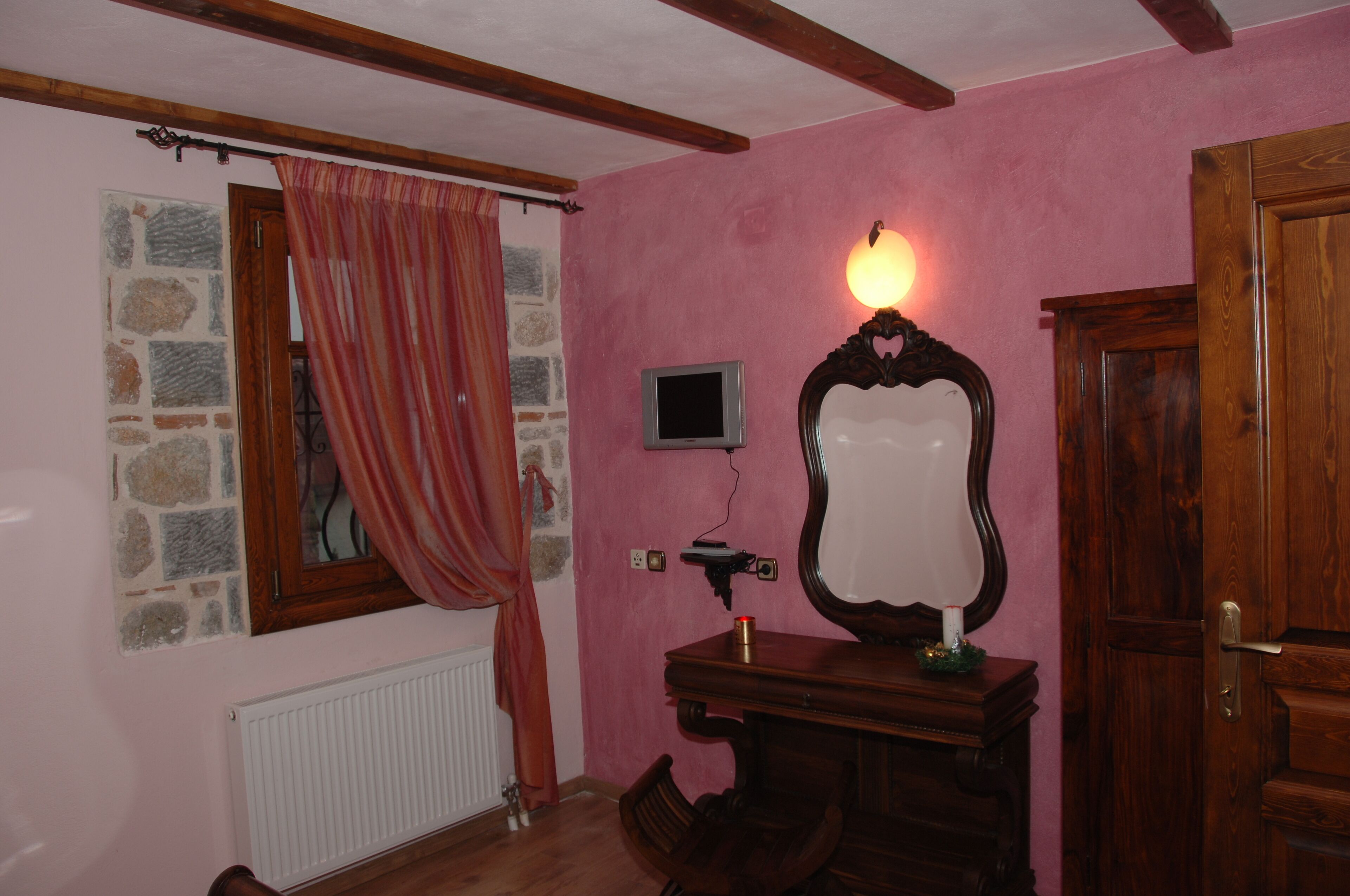 A room with pink walls, a stone-framed window, a wooden dresser, a mirror, a small television, and a door.