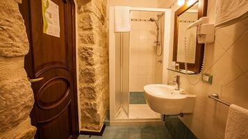 Un baño con pared de piedra, puerta de madera, ducha, lavabo y espejo con secador de pelo.
