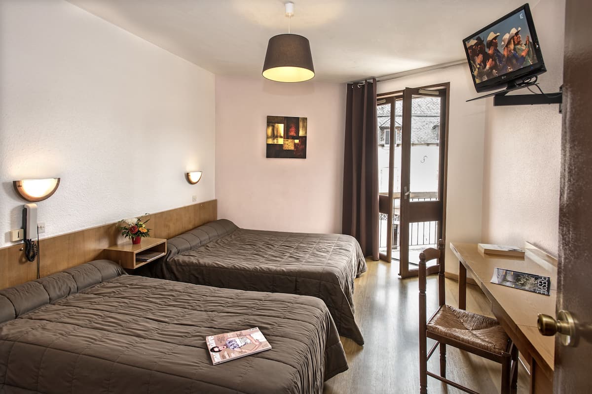 Ein Hotelzimmer mit zwei Betten, einem Schreibtisch, einem Stuhl, einem Fernseher und einem Fenster mit Vorhängen.