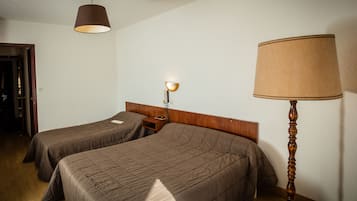 Ein Hotelzimmer mit zwei Einzelbetten, einem hölzernen Kopfteil, einem Nachttisch mit Lampe und Holzboden.