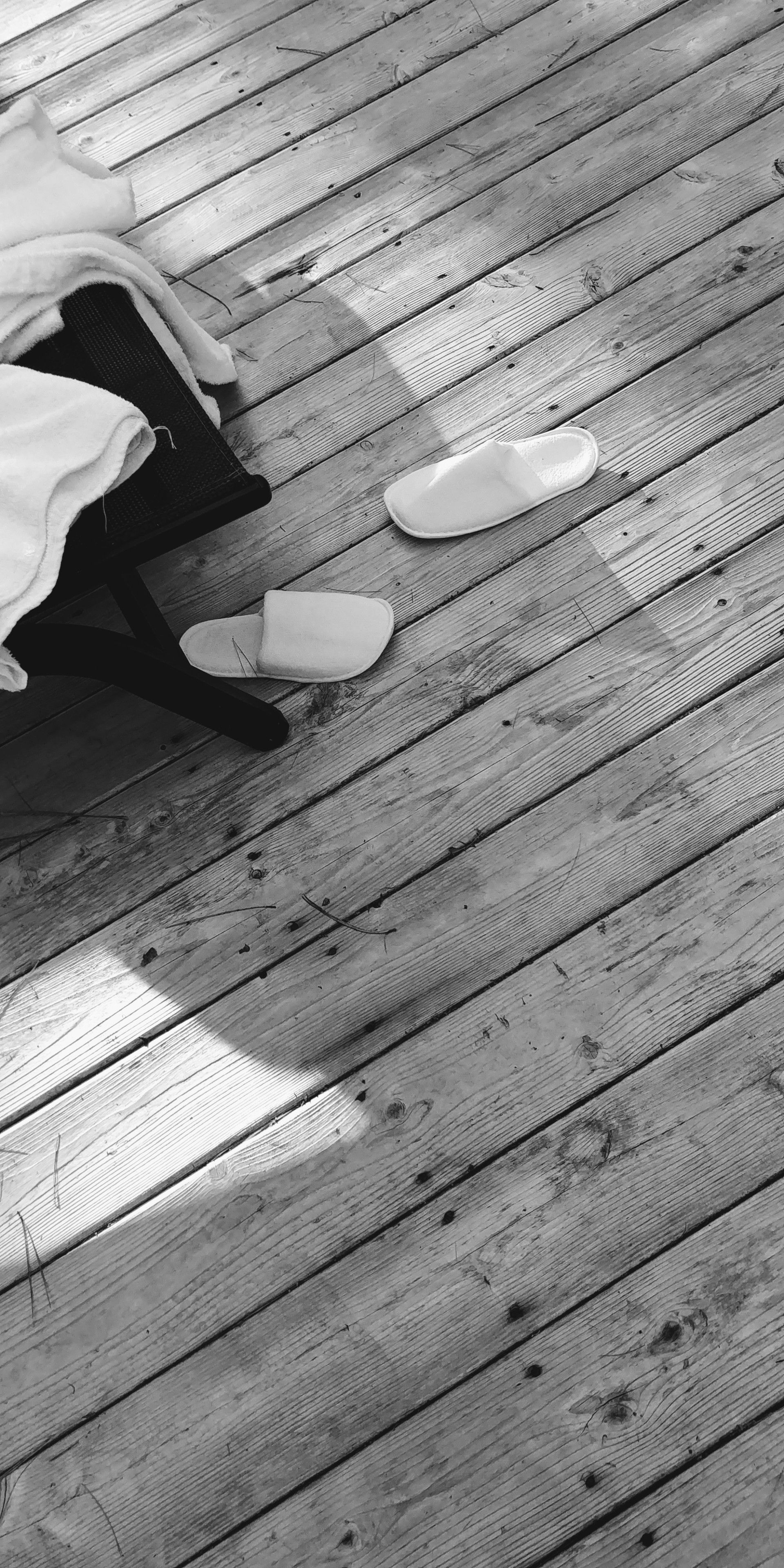 Un suelo de madera con un par de zapatillas y una manta sobre una silla.