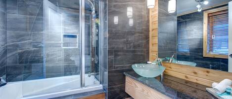 A modern bathroom with a glass-enclosed shower, a wooden vanity, and a large mirror.