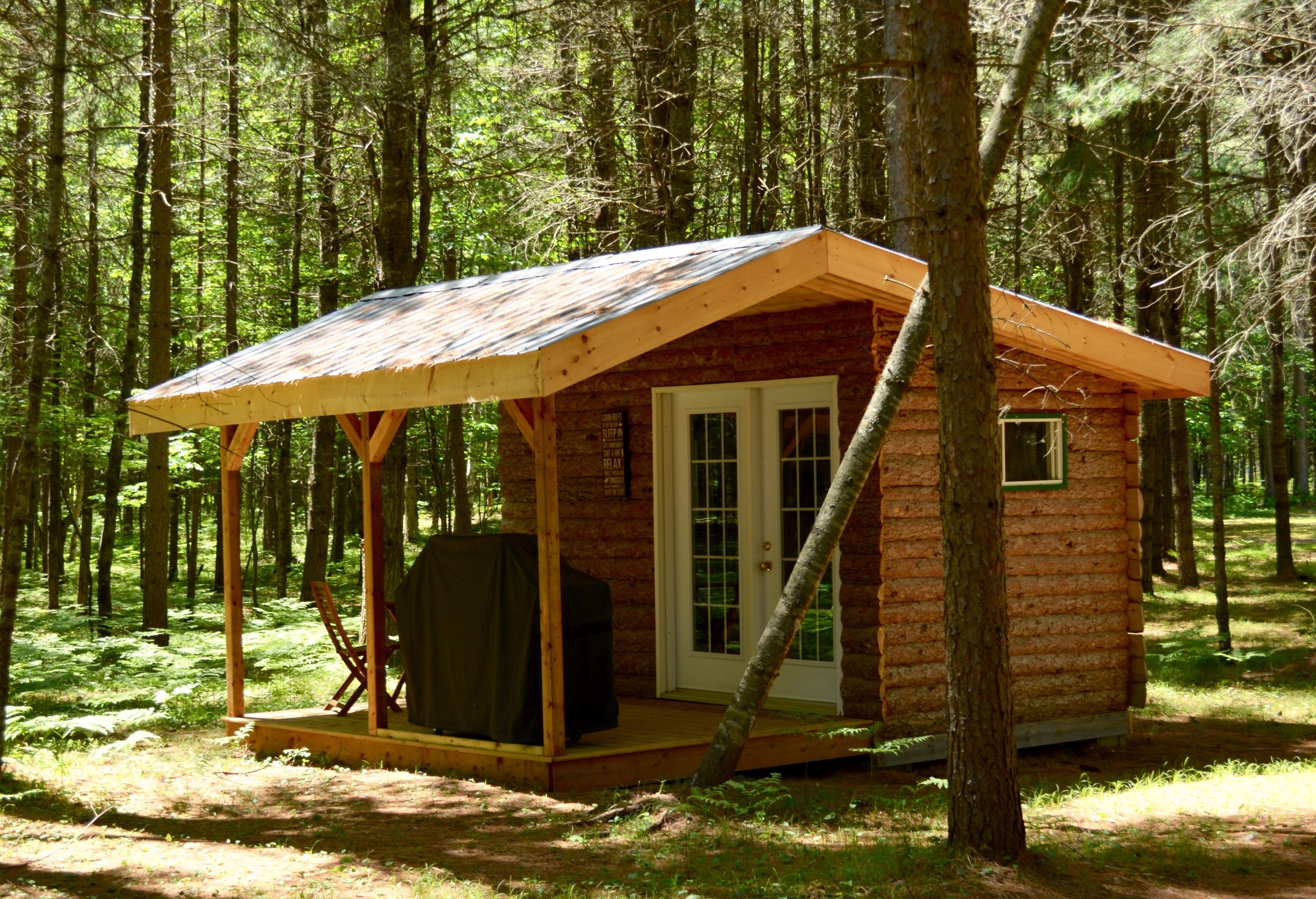 A small wooden cabin with a porch, a covered grill area, and a door with windows.