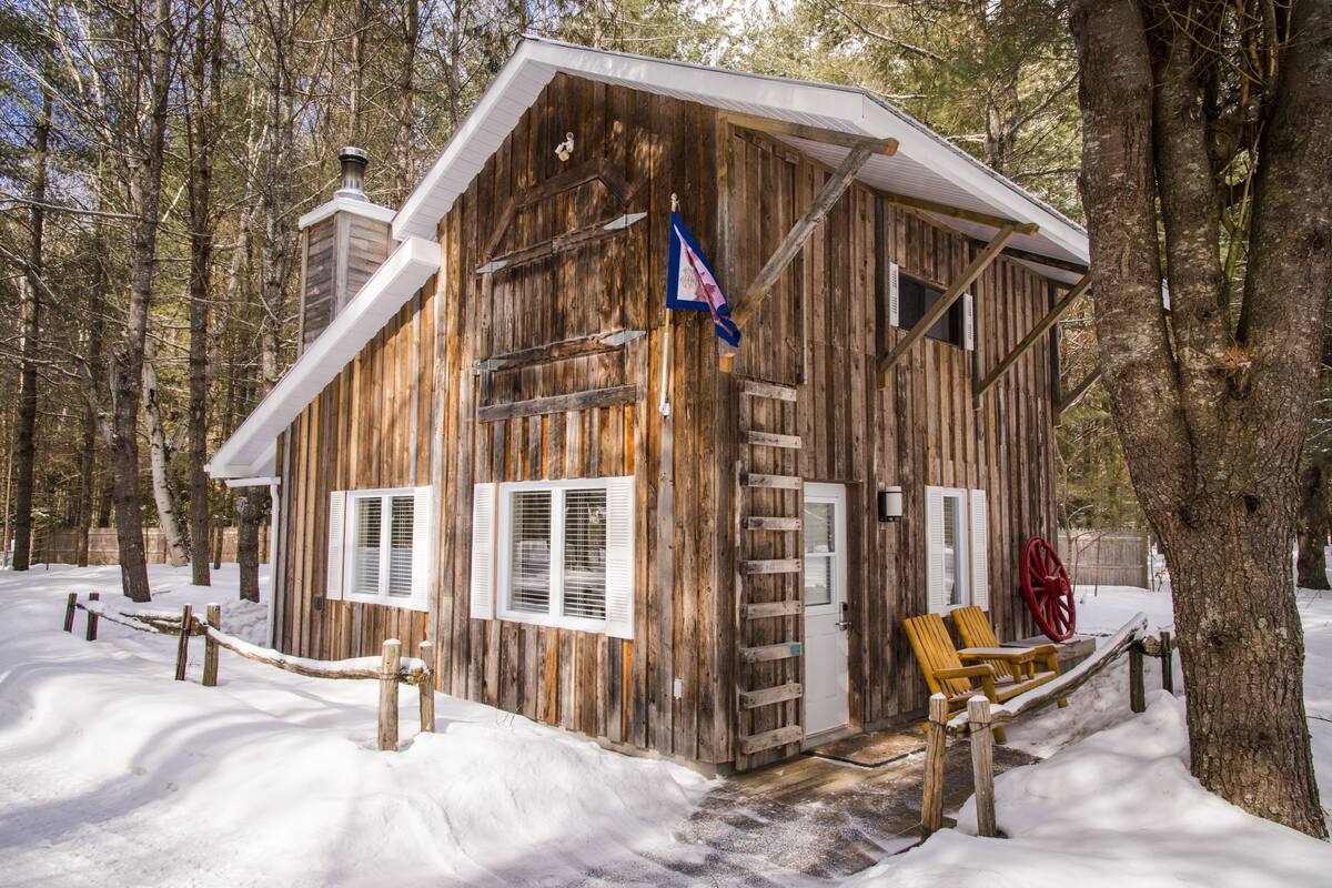 Une cabane en bois rustique, dotée d’une véranda, d’un drapeau et d’un banc.