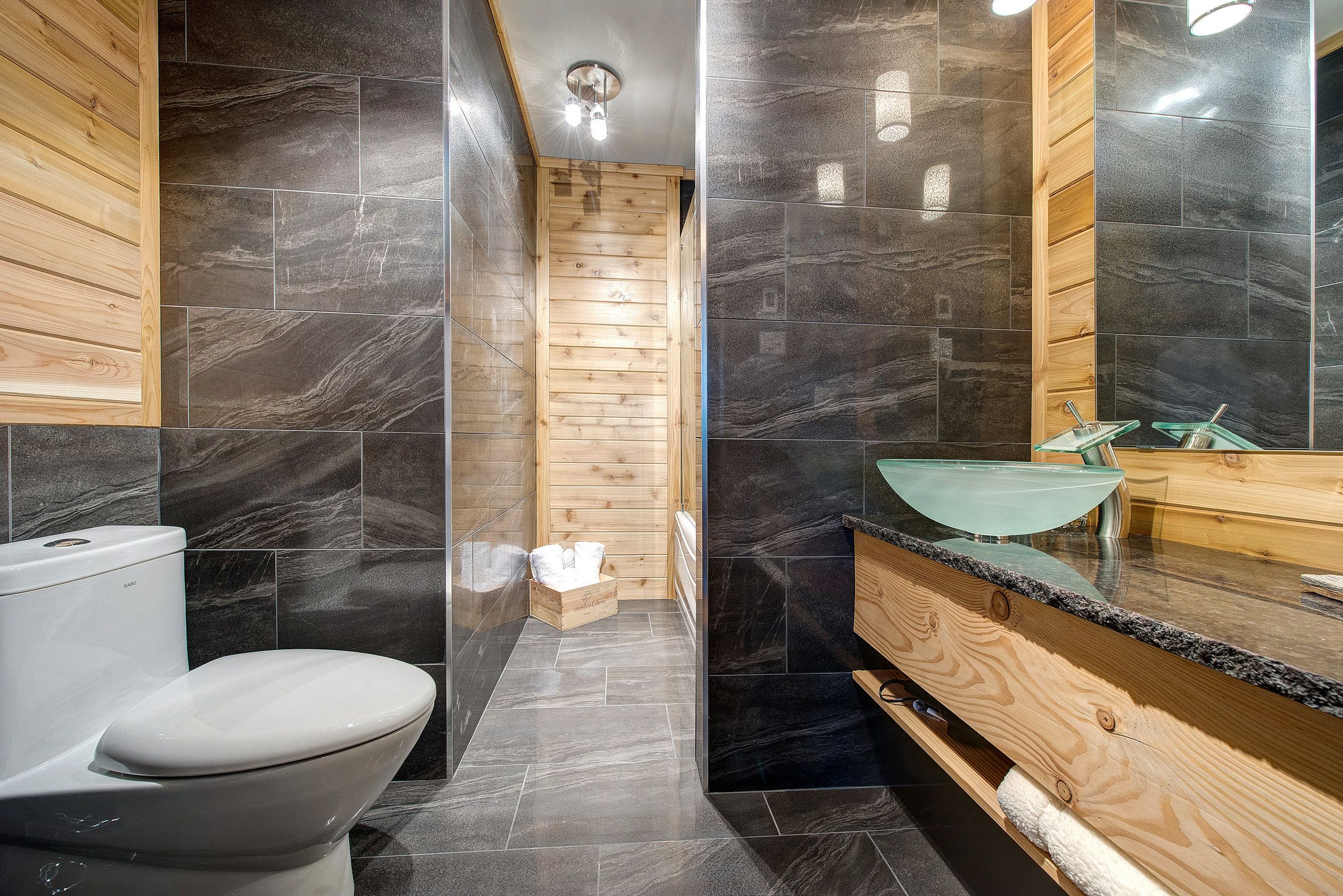 A modern bathroom with a wooden vanity, a glass sink, and a black marble backsplash.