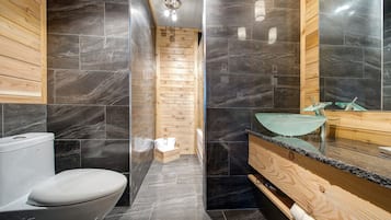 A modern bathroom with a wooden vanity, a glass sink, and a black marble backsplash.