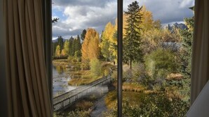 Blick durch ein Fenster auf eine natürliche Landschaft mit einer Brücke, Bäumen und Bergen.