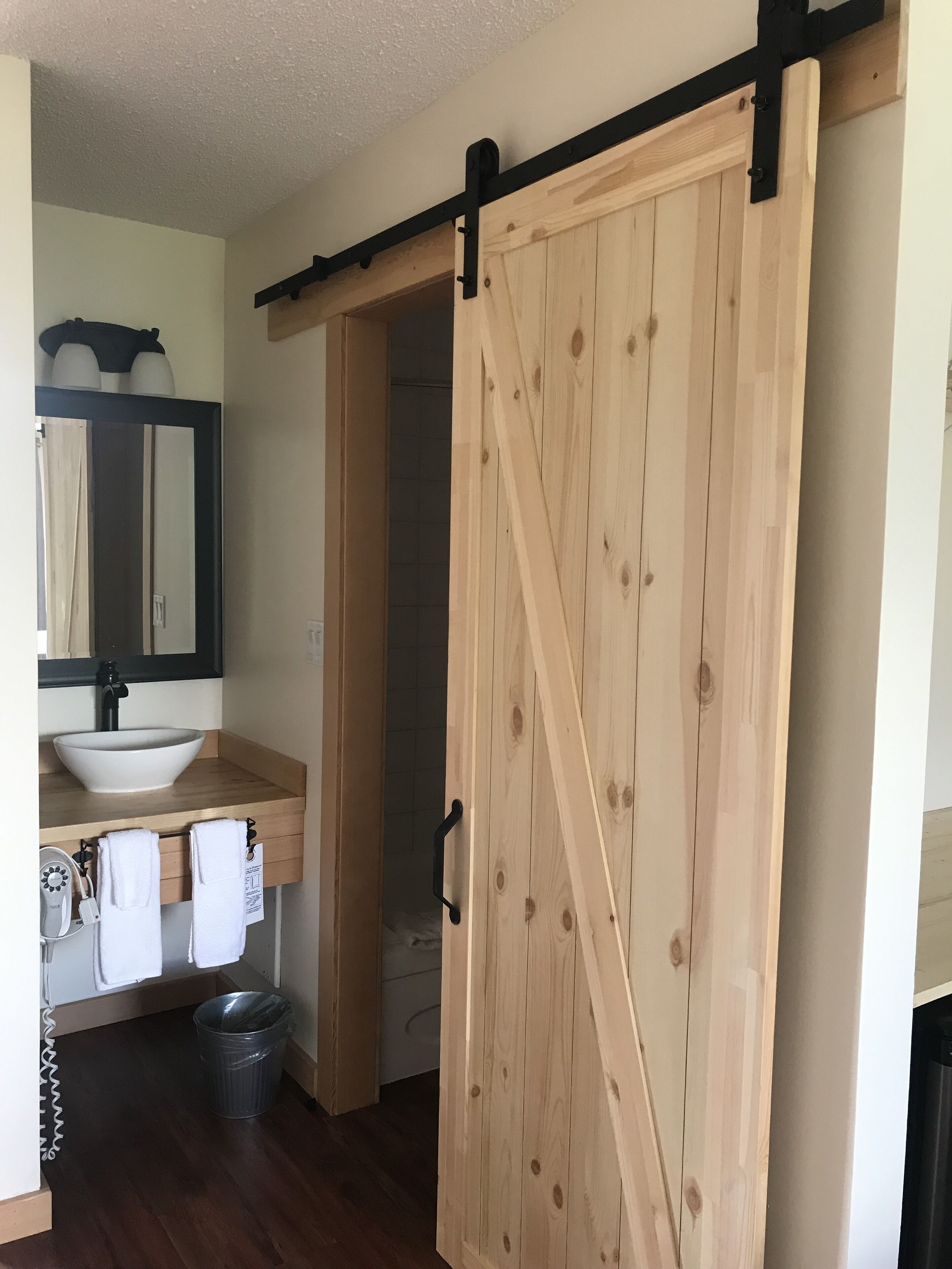 A bathroom with a wooden door, a sink, a mirror, and a towel rack.