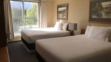 Habitación de hotel con dos camas, un ventanal con cortinas, un cuadro en la pared y una lámpara en la mesita de noche.