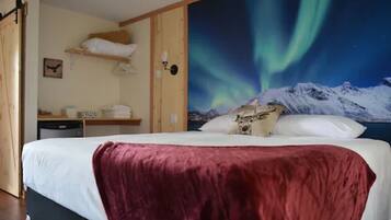 Un dormitorio con cama, mesita de noche, estante en la pared y un cuadro de las auroras boreales.