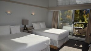 Ein Hotelzimmer mit zwei Betten, einem Nachttisch, einer Lampe und einem großen Fenster mit Blick auf Bäume.