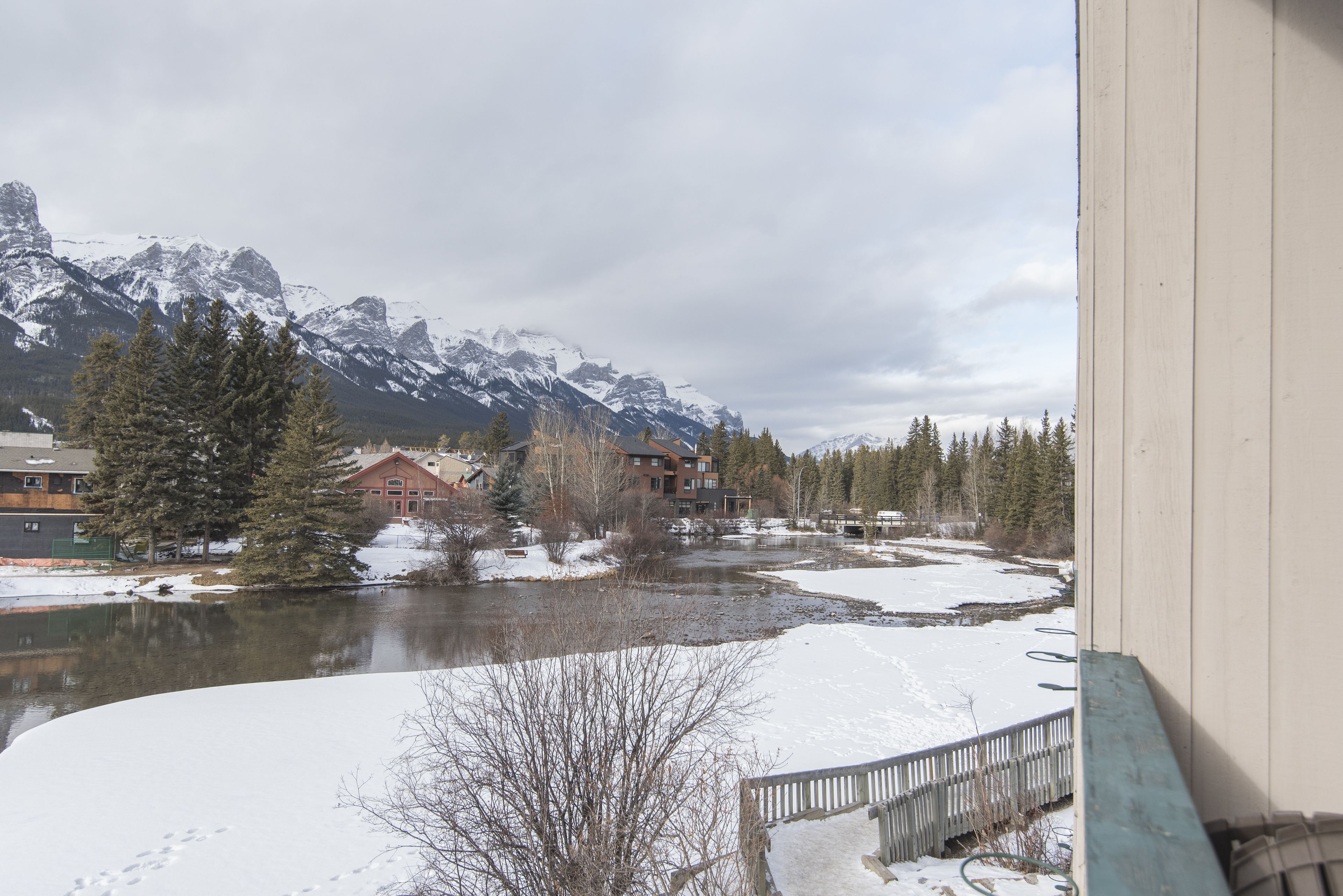 A view of a river with snow-covered banks, a wooden deck, and buildings in the background.