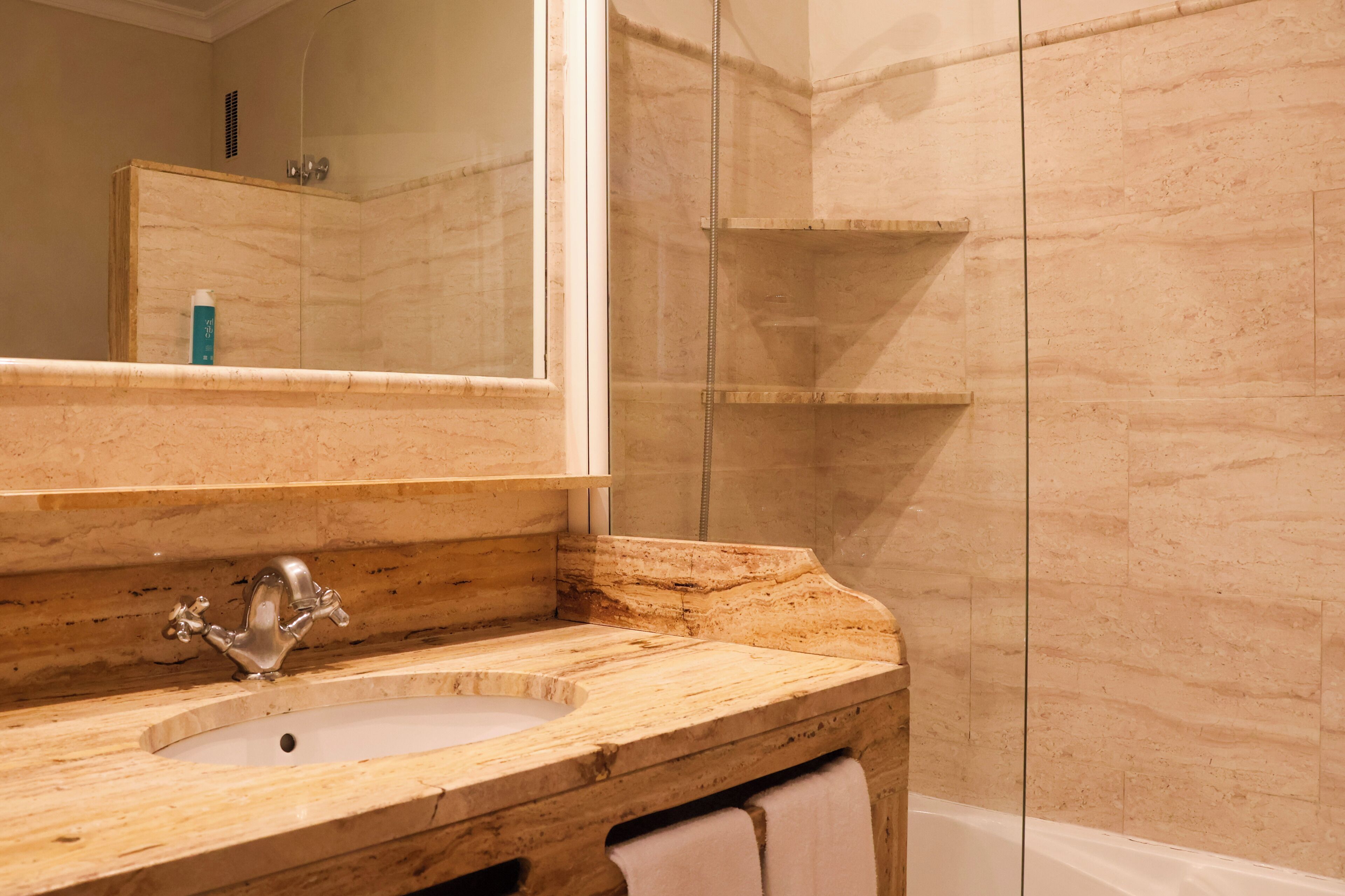 Un baño con lavamanos de mármol, espejo, ducha y toallero.