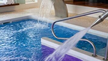 An indoor swimming pool with a waterfall feature and a view of the outdoors.
